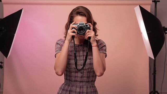 Young Woman Photographer Capturing a Shot with a Retro Film Camera in a Bright Studio with Pink Backdrop and Softbox Lights
