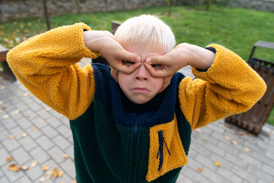 Child making playful face with hand goggles outside