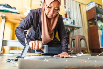 Asian seamstress ironing fabric in home workshop