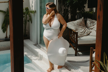 Caucasian female in white swimsuit and hat by pool in relaxing outdoor setting