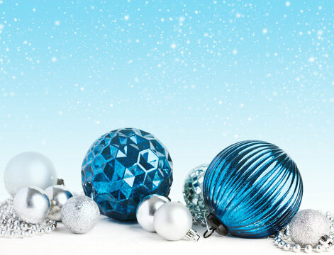 Close-up of various assorted blue and silver Christmas baubles with a festive snowy background 