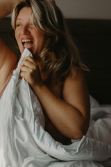 Caucasian female adult smiling in bed with white blanket during morning