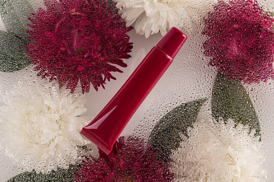 Red lip balm with aster flowers and water droplets