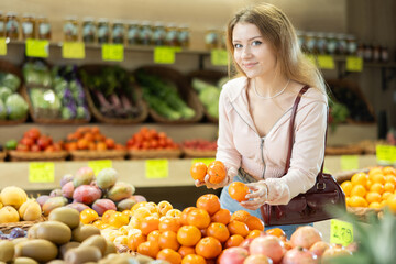 Smiling shopper selects ripe tangerine from the counter at a grocery store
