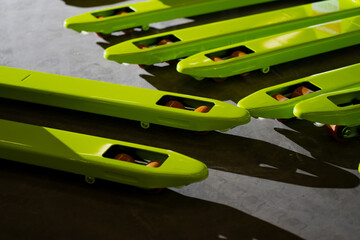 Close-up of green pallet jack forks aligned on warehouse floor showing metal rollers, industrial coating finish, and equipment detail used in logistics, warehouse transport operations