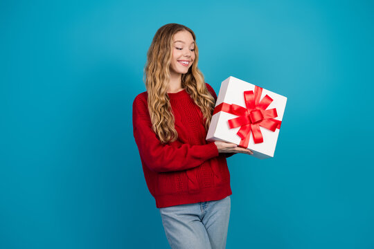 Charming young woman holding a beautifully wrapped gift box against a blue background showcasing festive joy - Powered by Adobe