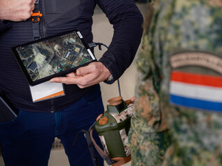 Military personnel using tablet with aerial mapping software during outdoor field training demonstration exercise