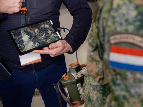 Military personnel using tablet with aerial mapping software during outdoor field training demonstration exercise