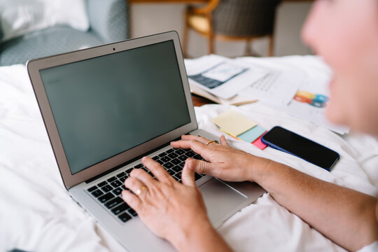 Freelancer woman typing on laptop with focused mindset, surrounded by papers, notes, and smartphone, representing mobile digital professionalism and organized workflow in remote setup.
