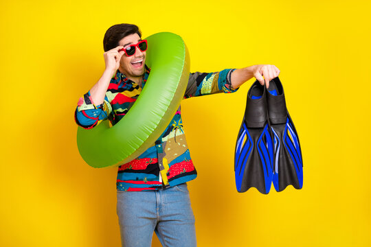 Young man in colorful shirt with green inflatable ring blue fins poses against bright yellow background for summer fashion - Powered by Adobe