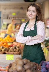 Woman seller in an apron stands in a farm store near a counter with fresh vegetables and fruits. Quality products in the vegetable section of the supermarket.