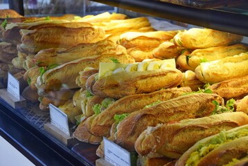 Traditional French bread with different fillings, sandwiches behind a glass display case.