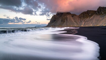 Dramatic Sunset Over Black Sand Beach With Crashing Waves And Jagged Mountains In The Background