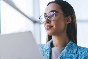 Close-up of confident businesswoman in glasses with tablet, reflecting light in lenses, symbolizing clear vision, tech fluency and digital focus in modern leadership.