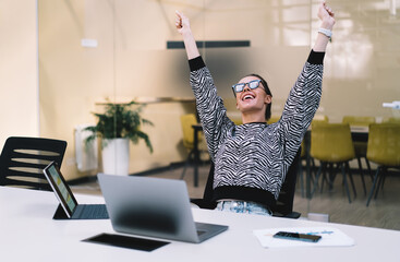 Smiling freelancer raises arms in triumph after completing task, representing confidence, digital...