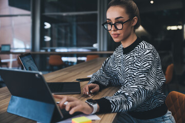 Young professional woman browsing tablet screen, confidently managing digital data across platforms, showcasing modern multitasking skills and mobile-first business mentality.