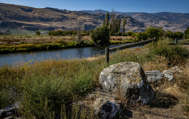Scenic view of a river flowing in a valley with large rocks in the foreground and mountains in the distance