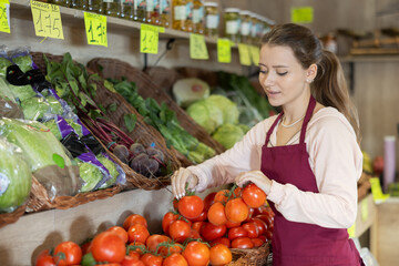 Woman seller working in supermarket and lays out fresh tomatoes on counter
