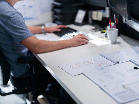 Professional reviewing architectural floor plans and blueprints at office desk with computer and documents