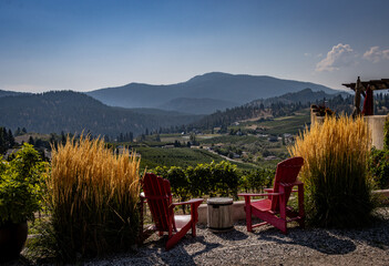 Scenic image of two red chairs overlooking a vineyard in a valley and mountains in the distance on a sunny day.