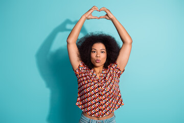 Young woman forms a heart with her arms against a blue background wearing a colorful patterned shirt