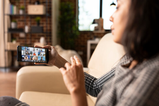 Woman entrepreneur seated with phone in hand, discussing with multiethnic professionals in online workshop. Close up of female manager using smartphone for video call with remote colleagues. - Powered by Adobe