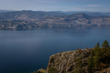 Scenic view of Lake Okanagan from high up on a mountain. The lake is calm and deep blue.
