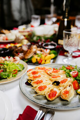 Festive crepe rolls with red caviar, greens and cherry tomatoes on elegant table setting