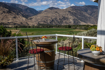 Scenic view of two chairs and a table made from a wine barrel overlooking a green valley and distant mountains.