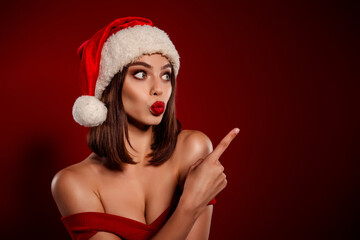 Glamorous young woman in Santa hat with bold red lips posing against festive red background Christmas fashion portrait