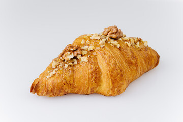 Golden croissant topped with caramel glaze and crunchy walnut pieces on white background