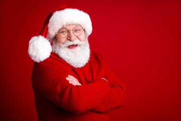 Naklejka premium Cheerful Santa in red sweater with hat and glasses smiles with arms crossed against a bold red background