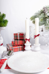 New Year's table setting with white plates, candles and decorative gifts. Red and green accents create a festive atmosphere.