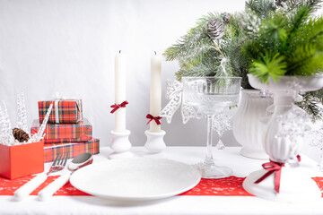 New Year's table setting with white plates, candles and decorative gifts. Red and green accents create a festive atmosphere.