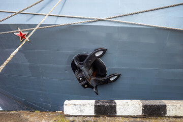 Large anchor on the side of a grey ship with red star emblem and mooring ropes © Dmitry