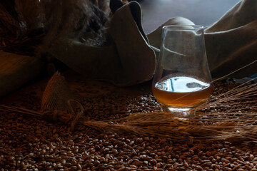 Rustic low-angle close-up of glass of amber whiskey, raw barley grain, wheat ears and burlap texture. Conceptual still life emphasizing heritage and natural ingredients of distilled spirits