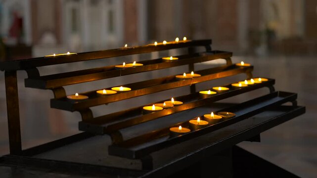 Votive candles burning in a church creating a spiritual atmosphere. Many small votive candles burning brightly on a tiered metal stand inside a dimly lit church, creating a spiritual atmosphere