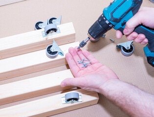 Close-up of a man's hands working with a cordless drill, assembling furniture.
