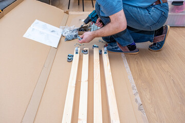 A Caucasian man using a cordless drill, assembling furniture.