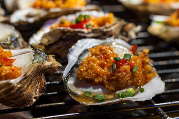 Guangzhou, Canton, China. close-up of grilled oysters topped with garlic, chili and scallions, traditional Chinese street food served hot on metal grill.
