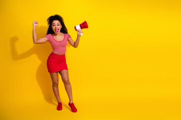 Cheerful young woman with a megaphone celebrating against a vibrant yellow background in a casual and trendy ensemble