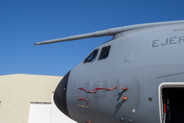 Forward fuselage of a tactical transport aircraft featuring the cockpit windows, refueling probe, and entry door under bright daylight
