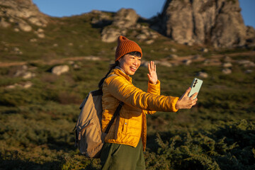 Fototapeta premium Woman hiking in mountains making video call on smart phone