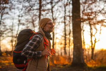 Mature man hiking in autumn forest at sunset