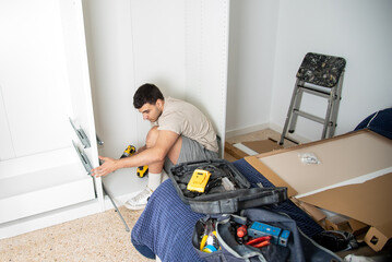 Young man assembling home furniture using power drill
