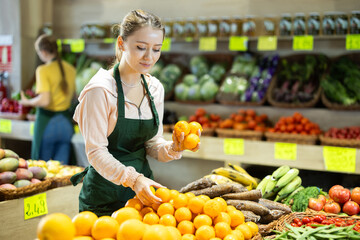 Girl employees in uniform holding fresh mandarines in grocery shop