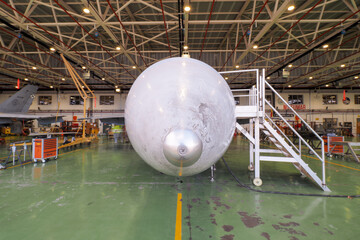Direct frontal view of the radome and extended nose landing gear of a twin engine multirole fighter jet in maintenance hangar