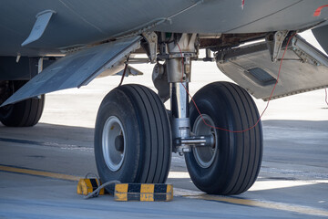 Detailed view of the aircraft nose landing gear showing dual wheels, hydraulic strut, and yellow-black wheel chocks on the tarmac