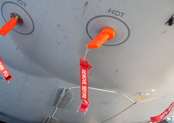 Orange protective plugs with red remove before flight tags installed on aircraft underside for ground safety