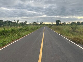 Empty asphalt road winding through the lush green countryside under a vast summer sky
